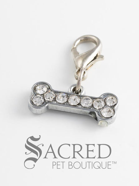 A silver charm with rhinestones in the shape of a bone and attached to a lobster clasp for attaching to a pet collar or as an accessory. On a white background with a grey Sacred Pet Boutique watermark.