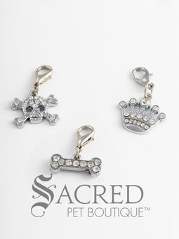 A collection of three different charms with rhinestones, including a skull and crossbones, a bone, and a crown, attached to lobster clasps for pet collars or accessories. On a white background with a grey Sacred Pet Boutique watermark.