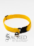 A yellow cat collar is set against a white background. The pattern on the collar looks like it is cracked. The collar has a black break away buckle and adjuster, as well as a silver bell on a silver split ring.