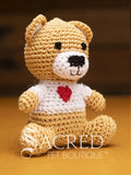 A cute crocheted fawn teddy bear wearing a white sweater with a love heart logo sits on a wooden table with a wooden wall behind. Suitable for small, toy and teacup dogs, the crochet toys squeak and will floss teeth as they play.