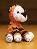 A cute crocheted tiger sits on a wooden table with a wooden wall behind. Suitable for small, toy and teacup dogs, the crochet toys squeak and will floss teeth as they play.