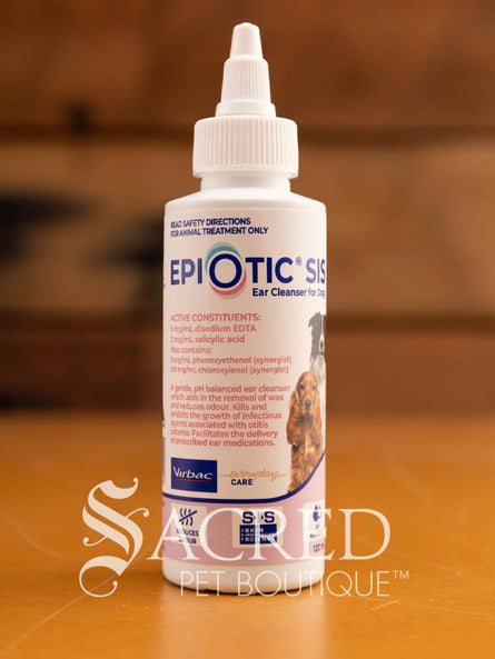 A bottle of Epi-Otic SIS ear cleanser for pets, with branding and instructions printed on the label, placed on a wooden surface. Features Sacred Pet Boutique watermark.