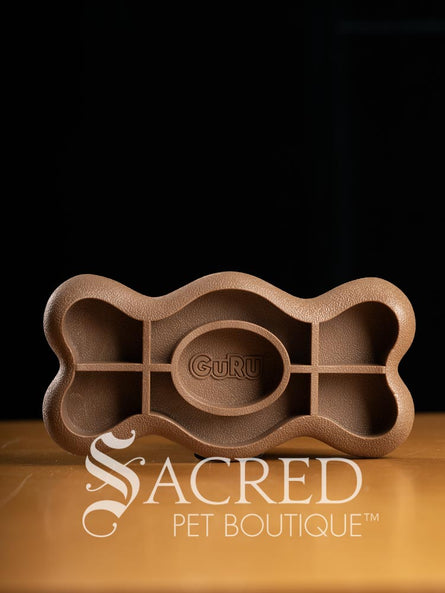 Brown bone-shaped treat dispensing and chewable dog toy with 'Guru' branding on a dark background, featuring 'Sacred Pet Boutique' logo.