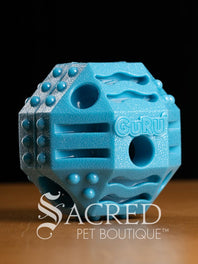 Blue, teal and yellow textured pet enrichment treat toys with 'Guru' branding on a dark background, featuring the 'Sacred Pet Boutique' logo.