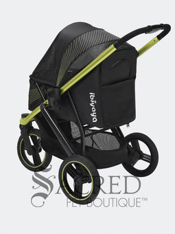 A woman in black athletic wear pushes a black pet stroller with green frame and wheel trim, in an outdoor urban setting. The stroller canopy has the brand name 'Ibiyaya' visible on the side. A white watermark from "Sacred Pet Boutique".