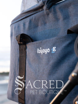 Pet stroller with a blue pet carrier on a paved path near a beach, featuring the Sacred Pet Boutique logo.