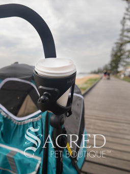 The Ibiyaya cup and phone holder is attached to a blue Happy Pet Stroller. and is being walked along a beach front. Hmm, coffee!
