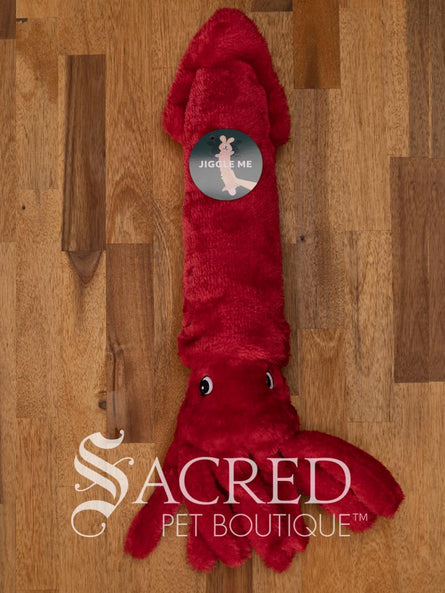 A bright red squid sits on a wooden table. It has embroidered eyes and short tentacles.