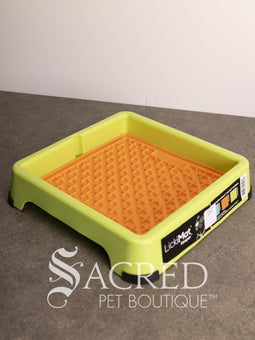A light blue LickiMat Keeper pet lick mat tray with its retail packaging insert, placed on a gray countertop against a white wall. A watermark for 'Sacred Pet Boutique' is visible at the bottom.