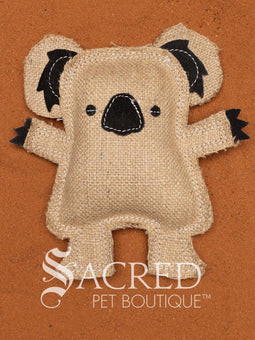 Kevin the Koala is a jute dog toy with wool felt detail and multiple rows of stitching, on a wooden background. A white Sacred Pet Boutique watermark.