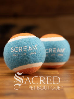 A single blue and orange tennis ball sits on a wooden table with a wooden background. The ball is solid foam, so it won't pop, has dog friendly fuzz and does not squeak.