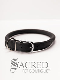 A black, round, soft leather dog collar with a metal buckle clasp. Our beautiful Soft Round (Rolled) leather collars are highly recommended for long haired dogs. Round or rolled collars reduce the amount of matting, tangling and flattening of the dogs fur. All collars are hand made and stitched with wax thread, from the finest quality soft leather wrapped and stitched around a nylon inner cord for added strength.Image on a white background, with the Sacred Pet Boutique logo.