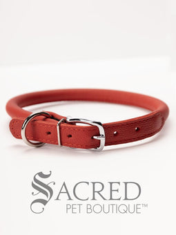 A black, round, soft leather dog collar with a metal buckle clasp. Our beautiful Soft Round (Rolled) leather collars are highly recommended for long haired dogs. Round or rolled collars reduce the amount of matting, tangling and flattening of the dogs fur. All collars are hand made and stitched with wax thread, from the finest quality soft leather wrapped and stitched around a nylon inner cord for added strength.Image on a white background, with the Sacred Pet Boutique logo.