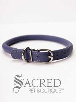 A black, round, soft leather dog collar with a metal buckle clasp. Our beautiful Soft Round (Rolled) leather collars are highly recommended for long haired dogs. Round or rolled collars reduce the amount of matting, tangling and flattening of the dogs fur. All collars are hand made and stitched with wax thread, from the finest quality soft leather wrapped and stitched around a nylon inner cord for added strength.Image on a white background, with the Sacred Pet Boutique logo.