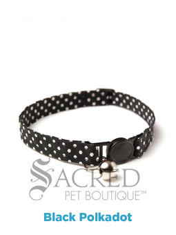 A cat collar is shown against a plain white background. The pattern of the fabric is pink with white polker dots. The collar has a black plastic breakaway buckle and adjuster, and a silver bell on a silver split ring.