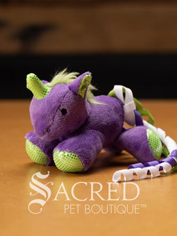 Three plush unicorn cat toys in different colours, each with a ribbon tail and glittery spots, placed on a wooden surface with a 'Sacred Pet Boutique' watermark.
