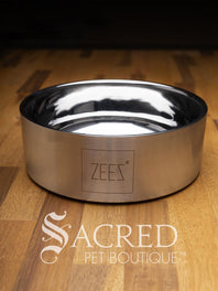A beautifully styled straight sided double walled steel bowl with brand name ZEEZ etched on the outer brushed finished edge shows the highly polished inner where the brand name is embossed on the base. Placed on a wooden table and watermarked with Sacred Pet Boutique.