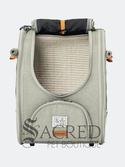 Person carrying a pet carrier with a cat inside, with a dog. surrounded by greenery, featuring the watermark 'Sacred Pet Boutique'.