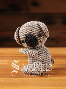 A cute crocheted panda bear stands on a wooden table with a wooden wall below. Suitable for small, toy and teacup dogs, the crochet toys squeak and will floss teeth as they play.