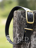 A black Biothane waterproof flat collar with brass buckle and a brass D ring for leash attachment, displayed on a wooden post. With a Sacred Pet Boutique Watermark. 