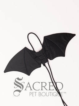 The Small size black bat costume wings sit on a white background. A loop at the top goes over the dogs head allowing the wings to sit over the dogs shoulders or wherever you think it looks best. The tails of the loop allow the head loop to be pulled longer or shorter and can then be tied under the dogs belly, or around its harness. 
