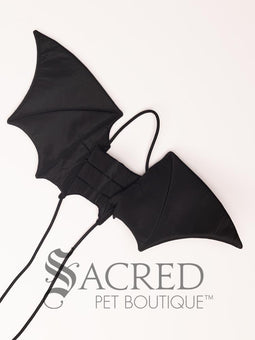 The Small size black bat costume wings sit on a white background. A loop at the top goes over the dogs head allowing the wings to sit over the dogs shoulders or wherever you think it looks best. The tails of the loop allow the head loop to be pulled longer or shorter and can then be tied under the dogs belly, or around its harness. 