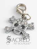 A silver charm with rhinestones in the shape of a skull and crossbones and attached to a lobster clasp for attaching to a pet collar or as an accessory. On a white background with a grey Sacred Pet Boutique watermark.