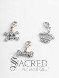 A collection of three different charms with rhinestones, including a skull and crossbones, a bone, and a crown, attached to lobster clasps for pet collars or accessories. On a white background with a grey Sacred Pet Boutique watermark.
