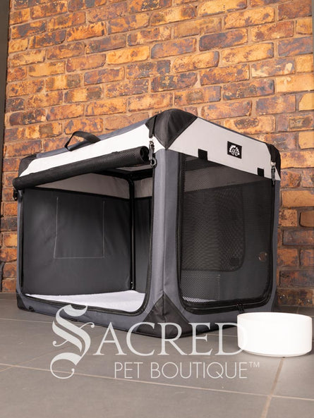 A Canine Care portable soft crate sits on a tile floor in a brick walled room. The side door has been rolled up. A white water bowl sits to the right of the crate. A white sherpa lining is inside the bottom of the crate. The crate looks spacious and airy.