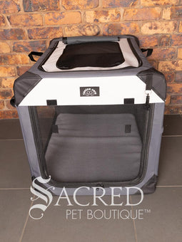 A Canine Care portable soft crate sits on a tile floor in a brick walled room. The side and an end door have been rolled up. An Italian Greyhound (it's Rossi) sits inside and looks to a person off screen. The crate looks spacious and airy.