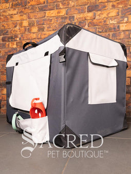 A Canine Care portable soft crate sits on a tile floor in a brick walled room. The side and an end door have been rolled up. An Italian Greyhound (it's Rossi) sits inside and looks to a person off screen. The crate looks spacious and airy.
