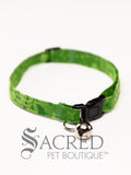 A cat collar is shown against a plain white background. The pattern of the fabric fades from mid to pale green, with a mix of darker and paler green leaves and buds. The collar has a black plastic breakaway buckle and adjuster, and a silver bell on a silver split ring.