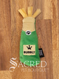 A plush cat toy shaped like a green bubbly bottle with yellow fabric mimicking a cork with yellow streamers at the top. The main body is green and has a central beige label with a black crown symbol on top of the word BUBBLY. There is a black label on the side that reads Zippy Claws with a white Sacred Pet Boutique watermark at the bottom of the image.
