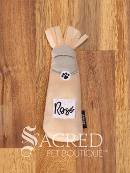 Three bottle shaped plush cat toys resting on a rustic wooden background. From the left there is a Rose, then a Whiskey and then Bubbly bottle. All three toys feature a fringed fabric top, a bottle shaped body and a black Zippy Claws label on the side. There is a white watermark of Sacred Pet Boutique at the bottom of the image. 