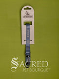 A blue Catventure cat leash with a metal clip, attached to a cardboard hanger, set against a solid olive green background with a 'Sacred Pet Boutique' watermark at the bottom.