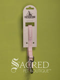A pink cat leash with a silver metal clasp, attached to a kraft cardboard hanger card branded CATVENTURE, set against a solid olive green background. With a white Sacred Pet Boutique logo.