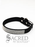 A black faux suede dog collar with sparkling rhinestone accents and a rhinestone-encrusted buckle on white background and Sacred Pet Boutique watermark.