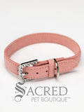 A pink faux suede dog collar with sparkling rhinestone accents and a rhinestone-encrusted buckle on white background and Sacred Pet Boutique watermark.
