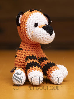 A cute crocheted panda bear stands on a wooden table with a wooden wall below. Suitable for small, toy and teacup dogs, the crochet toys squeak and will floss teeth as they play.