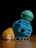 Blue, teal and yellow textured pet enrichment treat toys with 'Guru' branding on a dark background, featuring the 'Sacred Pet Boutique' logo.