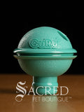 Turquoise teal treat dispensing pet toy with 'GURU' branding on a dark background, featuring 'Sacred Pet Boutique' logo.