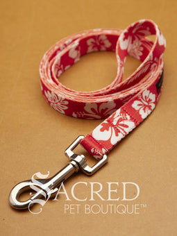 A red and white floral patterned pet leash with a silver metal clasp, displayed on a textured tan background with the 'Sacred Pet Boutique' logo overlay.