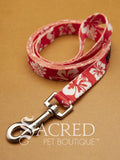 A red and white floral patterned pet leash with a silver metal clasp, displayed on a textured tan background with the 'Sacred Pet Boutique' logo overlay.