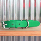 A orange biothane collar with stainless steel hardware thats buckled and lying a wooden shelf with a corrugated background. With a grey Sacred Pet Boutique watermark.