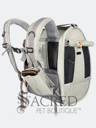Person carrying a pet carrier with a cat inside, with a dog. surrounded by greenery, featuring the watermark 'Sacred Pet Boutique'.