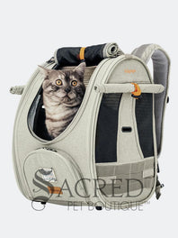 Person carrying a pet carrier with a cat inside, with a dog. surrounded by greenery, featuring the watermark 'Sacred Pet Boutique'.