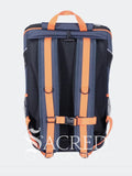 The back view of a navy blue and orange backpack, featuring adjustable orange shoulder straps, and a top carry handle, shown against a light grey background.
