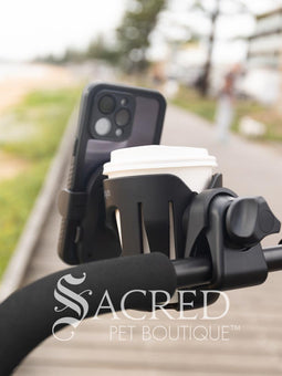 The Ibiyaya cup and phone holder is attached to a blue Happy Pet Stroller. and is being walked along a beach front. Hmm, coffee!