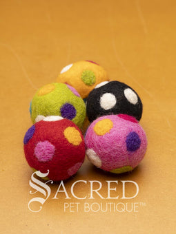 A pile of colourful wool felt balls with polka dots sits on a wooden table. Suitable for all cats and small to teacup sized dogs.
