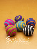 A pile of colourful wool felt balls with spirals contrasting colours sits on a wooden table. Suitable for all cats and small to teacup sized dogs.